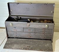 Full view of the large metal machinist tool chest with multiple drawers and open top compartment containing various tools including metal hammers.