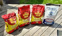 Four bags of charcoal on wooden deck, three Royal Oak Classic and one Kingsford The Original.