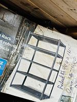 Photo of damaged retail box with an image of the metal rack showing four shelf levels and black metal framing.