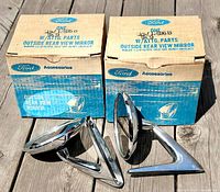 Pair of Ford OEM outside rear view mirrors with original Ford boxes, positioned on a wooden surface, showing front and side views of the mirrors and boxes.