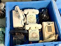 Six vintage landline phones with rotary and push-button dials in a blue plastic crate.