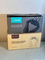Photo showing two boxes of the Shiatsu shoulder massagers, Naipo and Marnur brands, showing model numbers and features such as kneading and heat functions.