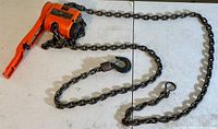 Full item showing the orange lever hoist with heavy lifting chain attached laid out on a white surface.