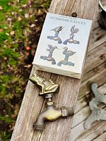 Image showing the solid brass frog-shaped outdoor faucet placed on a wooden surface next to the original box illustrating various brass faucet designs.