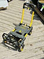 Full side view of Stanley folding truck on wooden deck showing the folded platform and handle upright.