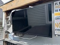 Front view of wall-mounted Amazon Fire TV under wooden pergola with grey cover partially draped