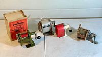Four vintage screw down pencil sharpeners shown in a row with one original Premier box on the left, all placed on a white surface against a light background.