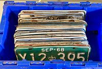 Bin full of vintage Ontario license plates, showing front plates with green and white colors and embossed characters with some rust and patina
