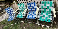 Four vintage folding lawn chairs with aluminum frames and woven webbed seats and backs in blue and green webbing, placed outdoors on grass.
