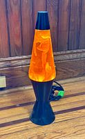 Full view of the orange tinted lava lamp showing glowing wax inside black base and capped top.