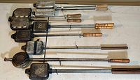 Seven vintage pie irons laid out showing variety of handle styles and metal compartments.