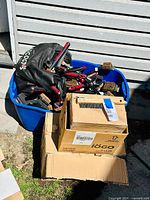 Large blue tote overfilled with black and red handled BBQ brushes alongside boxes containing smaller wire brushes.