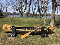 Starboard-side profile of yellow aluminum canoe on grass with paddle laid across