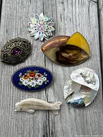 Top view showing all six brooches arranged on weathered wood, highlighting their colors, materials, and sizes.