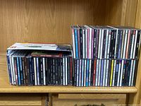 Photo showing a large assortment of CDs in jewel cases, stored on a wooden shelf in two rows.