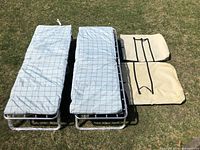 Two unfolded Coleman Bunkster cots with mattresses and two folded beige carrying cases arranged on grass