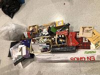 Overview of the entire craft lot including paints, brushes, knitting needles, markers, rubber stamps, and packaging materials laid out on the floor.