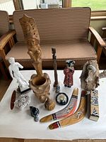 Overview of all decorative items on white table, including sculptures, boomerangs, carved artifacts, and painted figures.