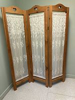 Front view of three wooden panels joined by hinges with white floral lace fabric inserts. Each panel has a heart-shaped cutout at the top.