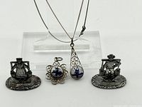 Full lot showing two silver figurines of Dutch people and two filigree pendants with Delft blue windmill designs, one teardrop pendant with chain and one flower-shaped pendant.