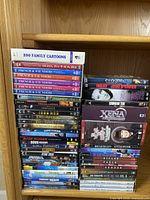 Photo of a large assortment of DVDs stacked on a wooden shelf including titles such as Lord of the Rings, Star Trek, French & Saunders, Xena, Dragon Heat Duo Denfer and others.