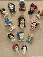 Front view of the shadow box frame showing all thirteen faces of famous ladies crafted in fabric and porcelain with unique hats and accessories.
