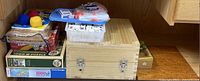 Assorted games and puzzle boxes stacked including 1000-piece Ravensburger puzzles and a wooden box for game storage