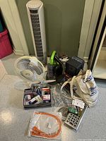 Full lot of household items including fans, upholstery cleaner, cords and hardware pieces shown together on floor