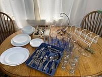 Photo shows complete dish and glassware set arranged on wooden table under window light.