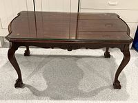 Front view of the mahogany claw foot coffee table with glass top protector, showing carved apron and claw feet.