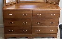 Front view of the maple dresser showing all six drawers with silver curved handles and the scalloped bottom edge detail.