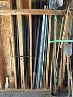 Wood-framed shed wall with black and silver steel T-posts upright between studs alongside shovels and broom
