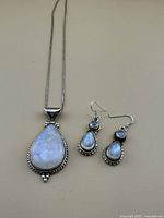 Full view of moonstone pendant and earrings on chain against plain background