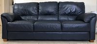 Front view of a navy blue leather sofa showing the full piece and cushions with some creasing.