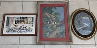 Three framed needlepoint art pieces including cats in window, house with garden path, and bridge scene, laid on tiled floor.
