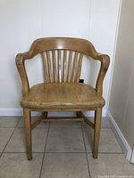 Front view of the oak banker's chair showing curved backrest, armrests, and seat wear.