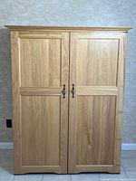 Closed oak cabinet with two paneled doors and metal handles, showing natural oak grain.