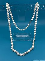 Full view of the pearl necklace hanging on clear stand showing overall length and clasp position