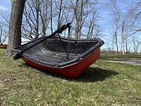 Angled side view on grass showing red exterior hull and black seating interior, tow bar resting on sled