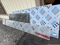 Corrugated polycarbonate roofing sheets leaning against exterior wall showing white and smoke panels
