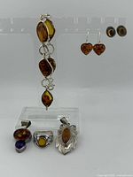 All items displayed on acrylic stand showing bracelet, earrings, studs, pendants and ring.