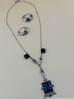 Full view of silver chain necklace with large black onyx pendant and matching black onyx hoop earrings on beige background.