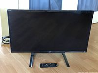 Front view of the Sony 32-inch flat panel TV on stand with remote placed in front.