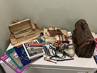 Overview of assorted stained glass supplies, instructional books, glass pieces, soldering iron, and tools arranged on a surface.