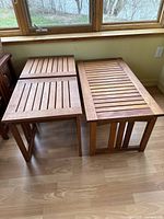 Top angled view of two square teak end tables and one rectangular teak coffee table placed side by side on a wood floor near a window showing their overall design and condition.