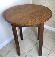 Side angled view of vintage oak round table showing oval tabletop with visible wood grain and four straight legs.
