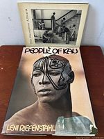 Two vintage art books are displayed layed on a wooden surface; 'People of Kau' by Leni Riefenstahl with a portrait on cover, and 'The Hampton Album' with a black and white photo cover