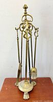 Full view of antique brass fireplace tool set on stand with lion paw feet.