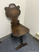 Photo of antique wooden chair showing high back with carved details and angled wooden seat