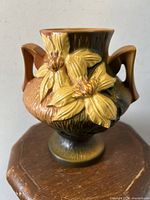 Front angle photo of Roseville Clematis vase showing two large yellow flowers in relief and brown textured body with handles